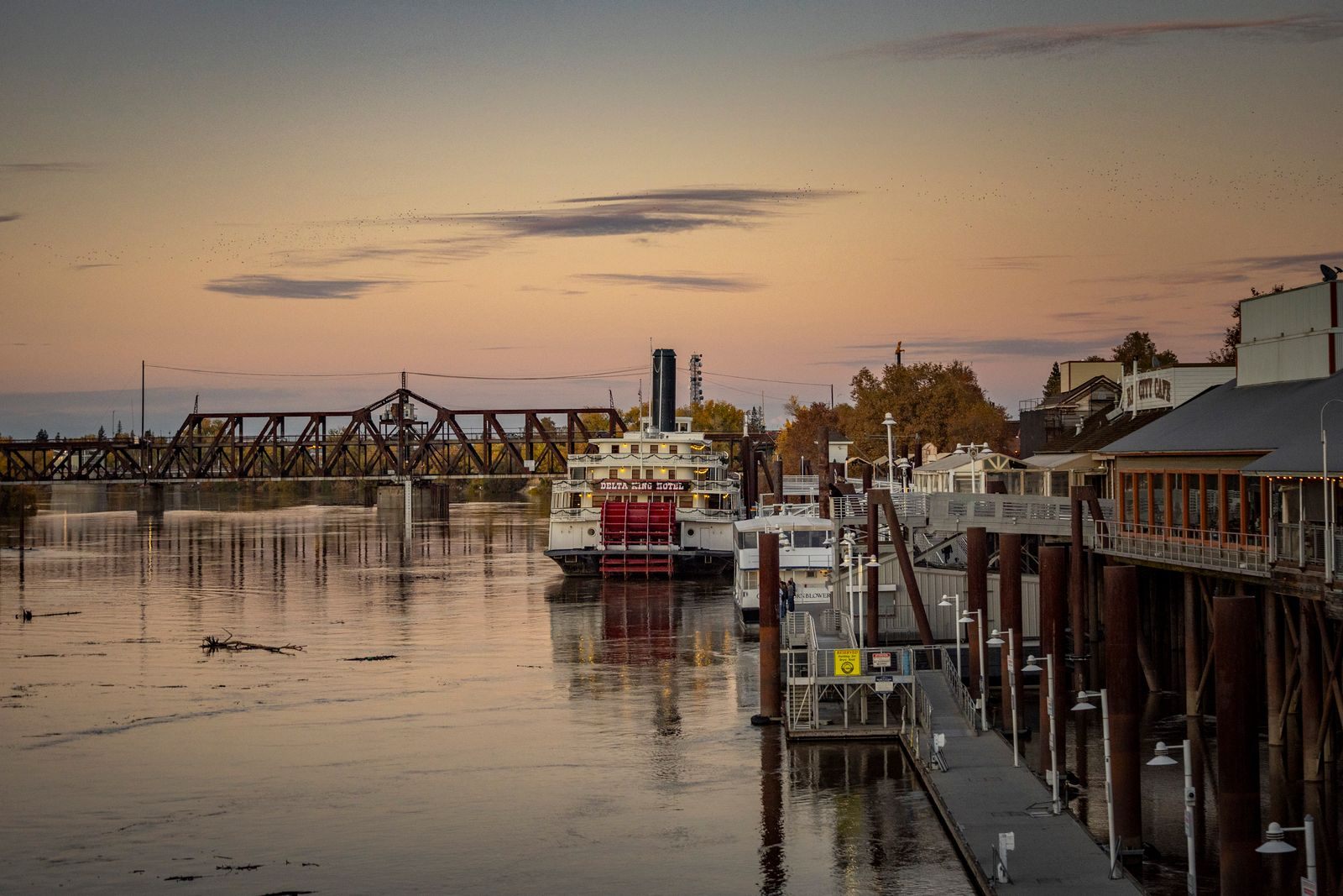 Classic sternwheel riverboat moored by a wooden wharf at sunset, ready for a sternwheeler riverboat cruise